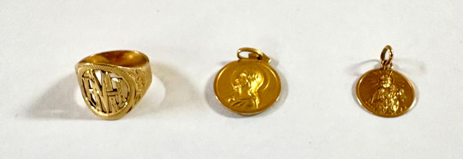 Anillo y dos medallas fotografiados sobre fondo claro